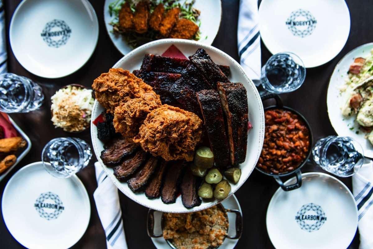 A barbecue platter with brisket, ribs, fried chicken, sides, cocktails, wine, and oysters
