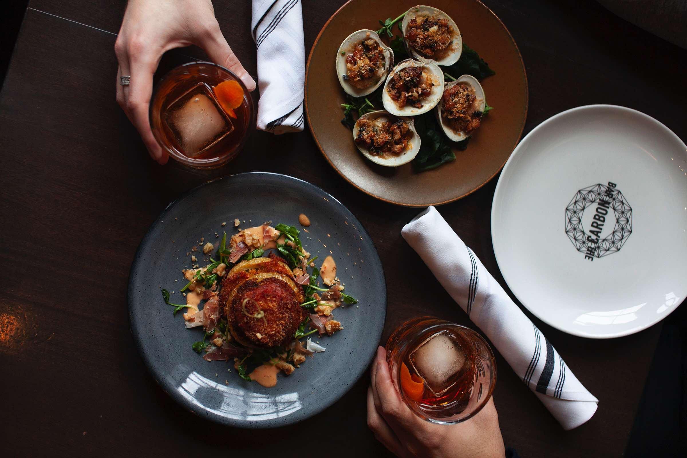 A table set with cocktails, sides, and live-fire mains at The Carbon Bar
