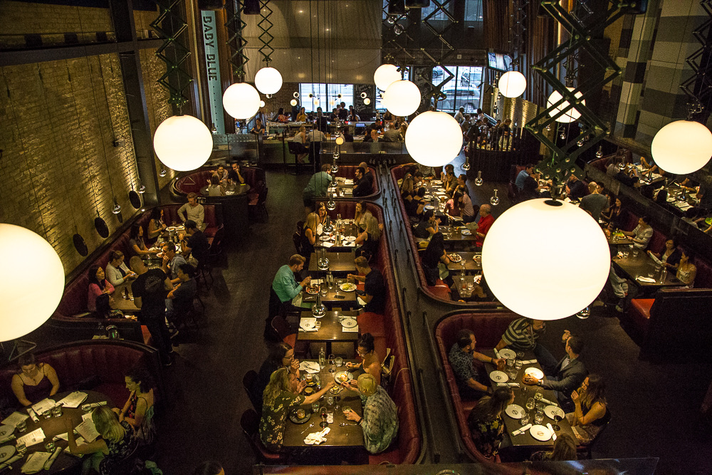 An eagle view of The Carbon Bar dining room with red leather banquettes, globe pendants, and set tables