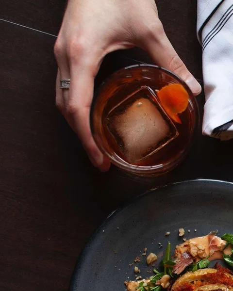 An amber cocktail over a large ice cube with orange peel at The Carbon Bar