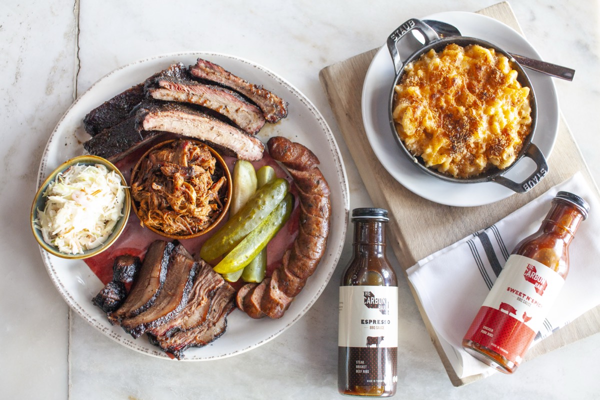 A Carbon Bar Pitmaster spread of brisket, ribs, pulled pork, sausage, mac and cheese, and Carbon Bar BBQ sauces from Shop The Carbon Bar